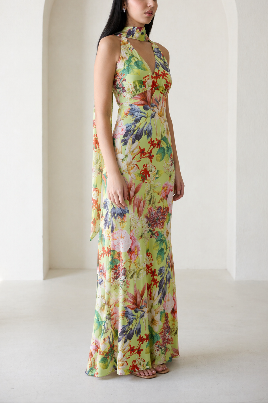 Woman wearing a colorful floral dress standing in a bright room with white walls.