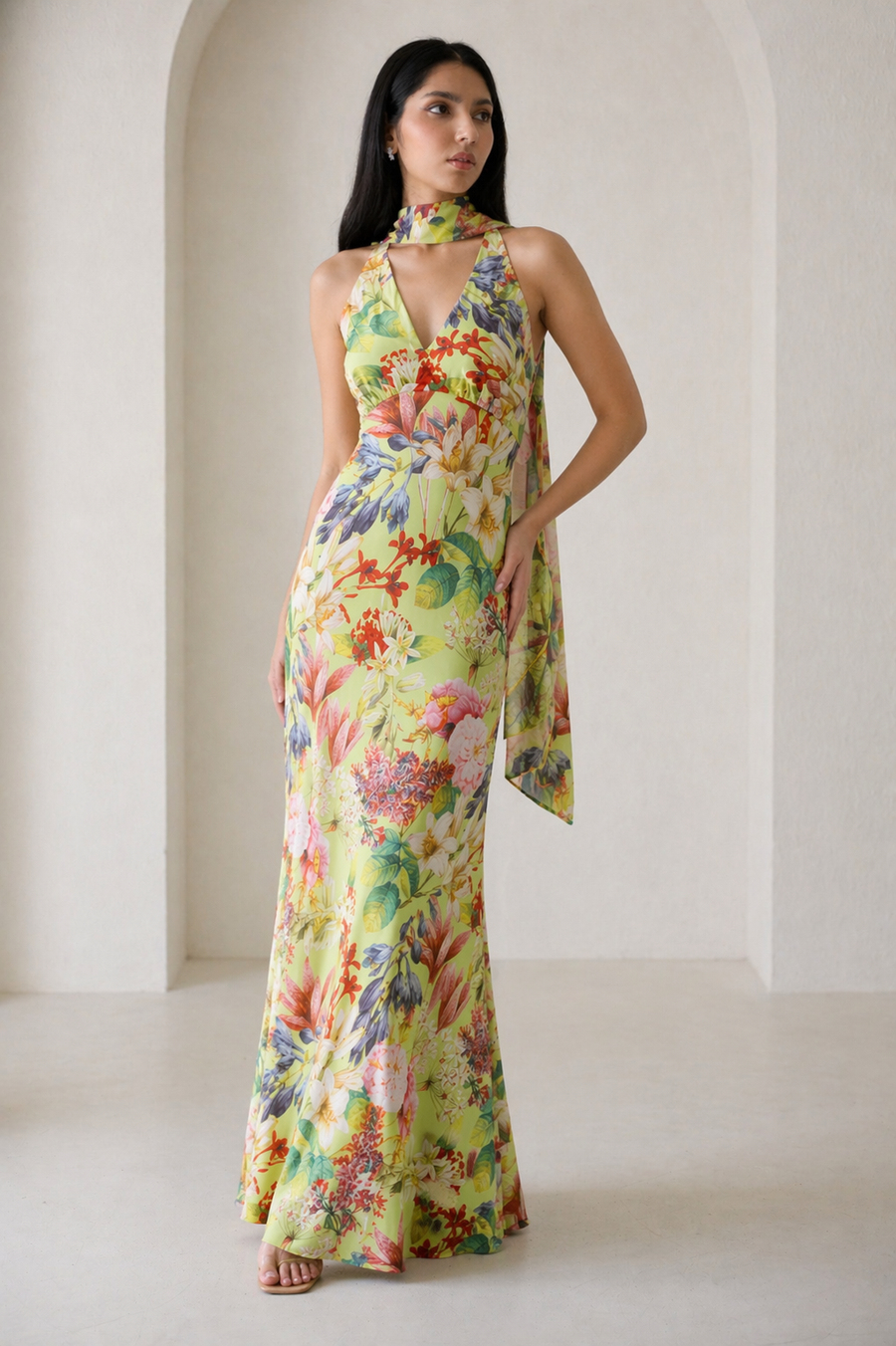 Woman wearing a colorful floral dress standing in a bright room with white walls.
